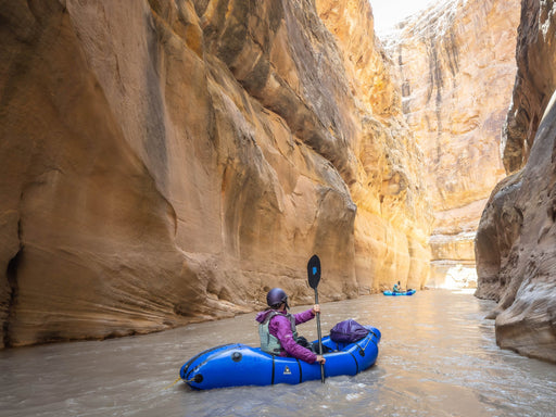 Two people in a blue kayak navigating a narrow canyon.